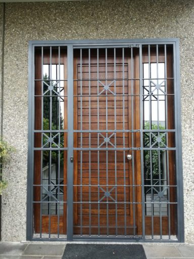 Porta in legno con inferriata decorativa, incorniciata da una parete di cemento.